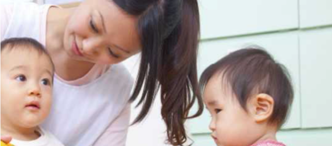 A woman kneeling beside two young children, engaging with them attentively.