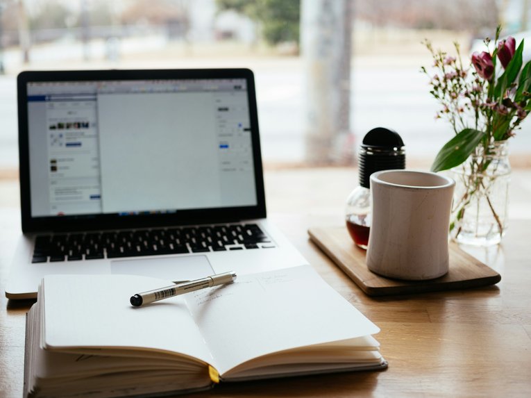 A computer screen next to coffee and flowers